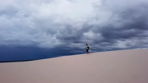 Guy walking alone in dunes of Lencois Maranhenses Stock Footage 168394423
