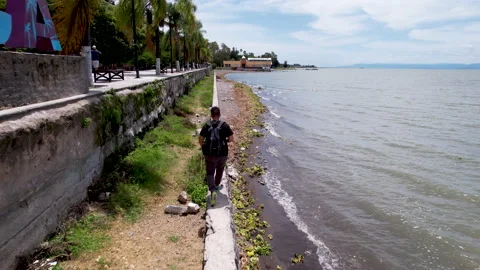 Guy walking along the shore of lake Chapala in Ajijic during sunny day Video stock 160234553