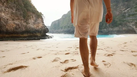 A guy is walking barefoot on the soft sand of a Kelingking beach in Bali 1st Stock Footage 126142872