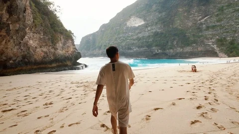 A guy is walking barefoot on the soft sand of a Kelingking beach in Bali 2nd Stock Footage 126142920