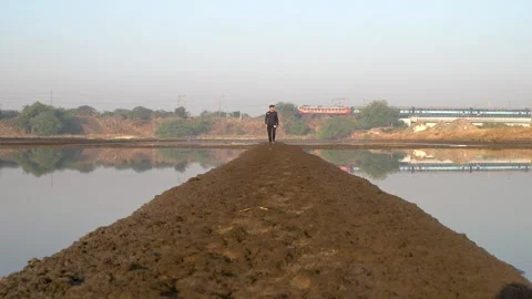Guy Walking On The Muddy Walkway Between Ponds In Mumbai, India With Local Vidéo 137908068