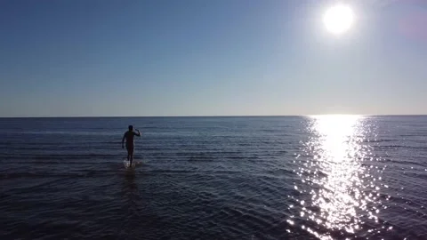 The guy is walking in shallow water towards the setting sun Stock Footage 180156747