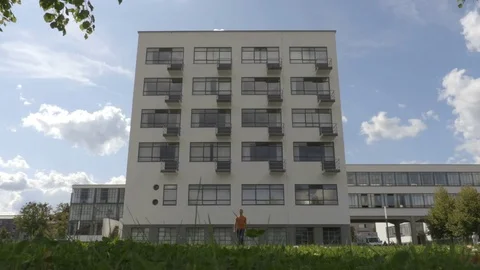 Guy is walking toward the camera with the Bauhaus building on the background Stock Footage 83634478