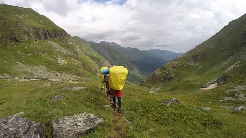 A guy walks along a mountain trail in a large backpack in a bright raincoat. Stock Footage 127734711