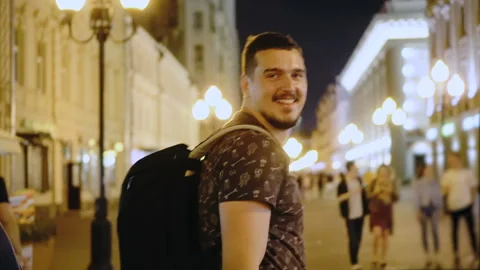 The guy walks down street of night city closeup and waves his hand follow me Stock Footage 102560311