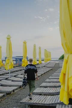The guy walks forward along the beach along the yellow umbrellas and deck cha Stock Photos