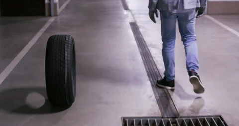 Guy walks parallel to rolling tire in underground garage Stockbeeldmateriaal 294610441