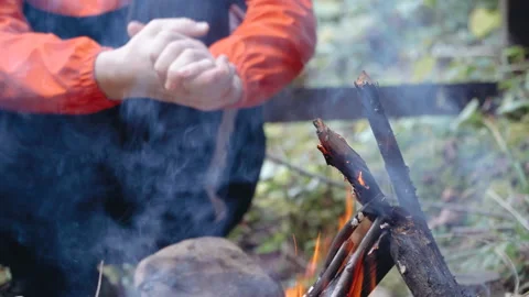 Guy warms his hands by the fire, surrounded by forest. Camp concept in forest. Stock Footage 195307990