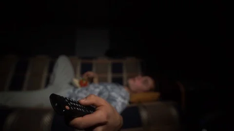 The guy watches TV, eats popcorn, switches channels, remote control in focus Stock Footage 126093323