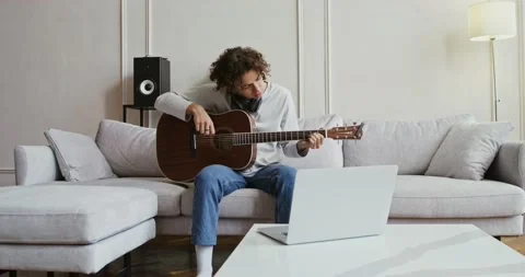 A guy watching guitar tutorial on laptop and learning to play instrument Stock Footage 161609245