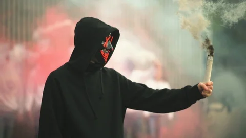 Guy wearing purge mask holding smoke bomb looking towards camera  Stock Footage