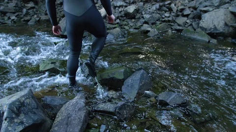 Guy in wetsuit crossing stream Stock Footage 96053020