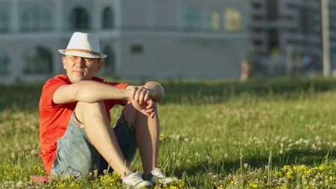 Guy in a white hat sits on the grass in a city park, camera movement Stock Footage 137645777