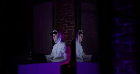 A guy in a white hooded sweatshirt sits at his computer in a dark room. hacker Stock Footage 132914151