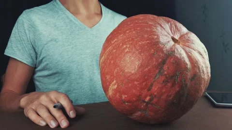 Guy in white shirt draws face on pumpkin jack o lantern with marker 4k Stock Footage 68305472
