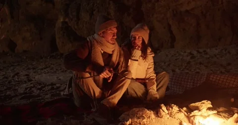 A guy in winter clothes and his girlfriend sit near a fire and cook a sausage on Stock Footage 308308048