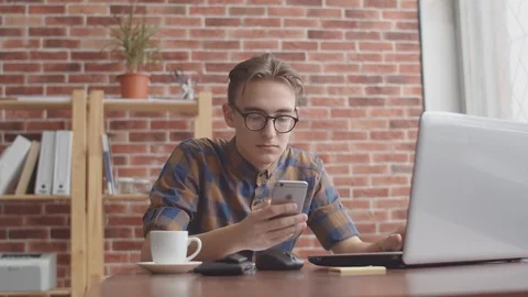 The guy is working on a laptop and holding a phone. A young blogger is typing on Stock Footage 125005477