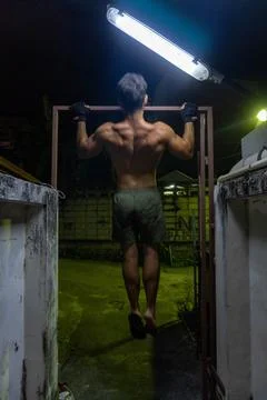 Guy working out in the street, doing pull-up, with neon lights. Stock Photos