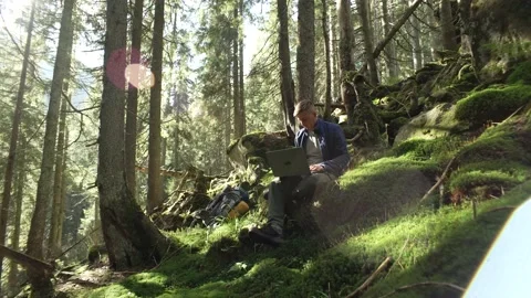A guy works at a computer in the forest while hiking in the mountains. Stock Footage 217396720