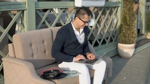 A guy writes with friends on a laptop on the veranda Stock Footage 87247231