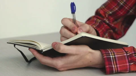 A guy writes notes in a notebook with a pen on a table Stock Footage 45440839