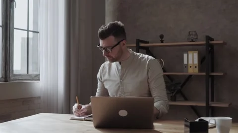 Guy writing in notebook while sitting at table and listening to teacher during Stock Footage 134449208
