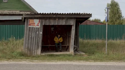 The guy in the yellow jacket is sitting alone at the bus stop and waiting for th Stock Footage 161302442