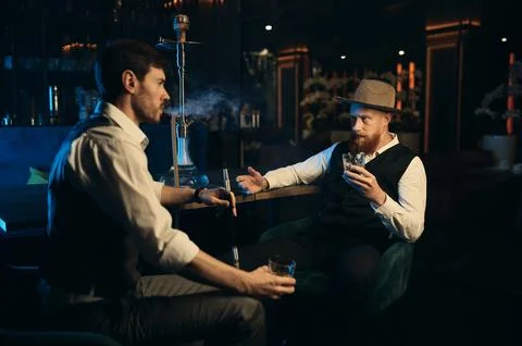 Guys having serious conversation while sitting face to face at hookah bar Stock Photos