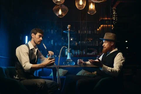 Guys having serious conversation while sitting face to face at hookah bar Stock-Fotos