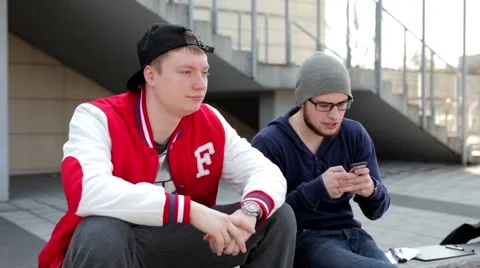 Guys sitting on the wall next to the building and looking into phone Stock Footage 49538439