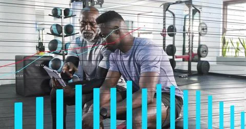 Gym coach tapping tablet, client leaning in reviewing data while teal bars Stock Photos