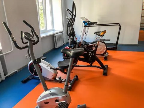Gym setting with elliptical, 2 treadmills, gray flooringwalls, orange accents Stock Photos