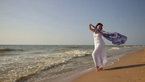 Gypsy young brunette girl wearing white maxi long dress standing near the sea or Stock Footage