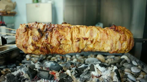 Gyros meat slowly roasting on a vertical skewer over glowing charcoal, preparing Stock Footage 343223002