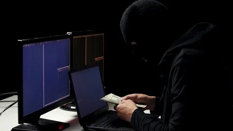 Hacker in balaclava cracking code using laptop and computers from his dark Stock Footage 74918974
