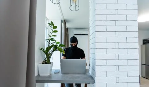 Hacker in black balaclava on a laptop Stock Photos