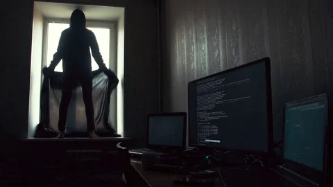 Hacker in black hood standing on the windowsill and covering windows with black Stock Footage 72324582