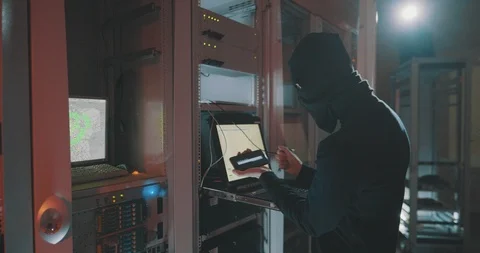 Hacker in black mask uses smartphone to crack server Stock Footage 107338697