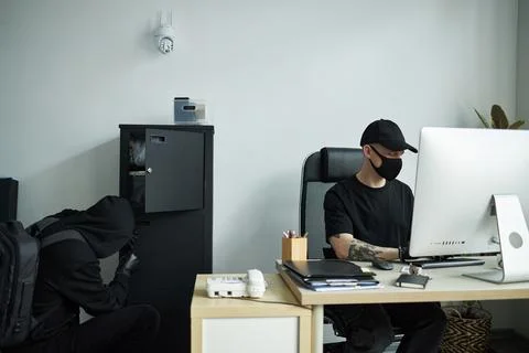 Hacker Breaking into Office Computer and Accomplice Raiding Safe Stock Photos