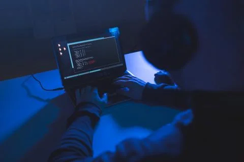 Hacker with coding on laptop computer in dark room Stock Photos