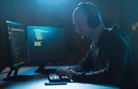 Hacker with coding on laptop computer in dark room Stock Photos