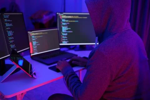 Hacker Coding at Multi-Monitor Desk in Neon Light Foto stock
