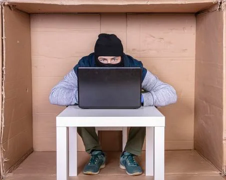Hacker covers his face while working on a computer.. Stock Photos