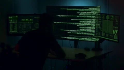 Hacker engaged in cyber attack, focused on multiple screens displaying code and Stock Footage 323322504