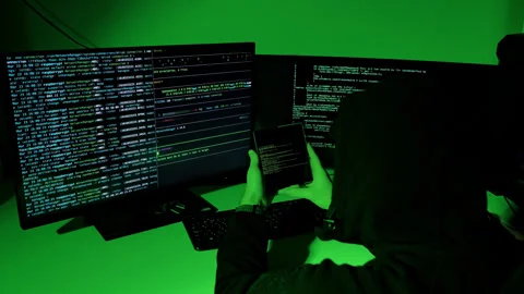 Hacker enters data from fold phone to keyboard in green-lit room, slow zoom-in Stock Footage 323045123