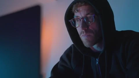 Hacker in front of a laptop putting glasses on and working. man in glasses and 스톡 동영상 332592601