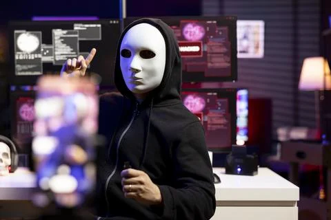 Hacker hidden in neon lit hideout films video ultimatum with smartphone Stock Photos