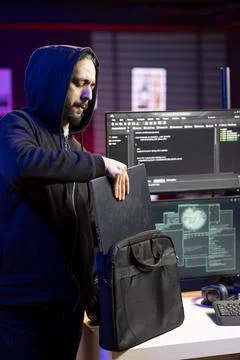 Hacker in hideout puts laptop in backpack after stealing sensitive information Stock Photos