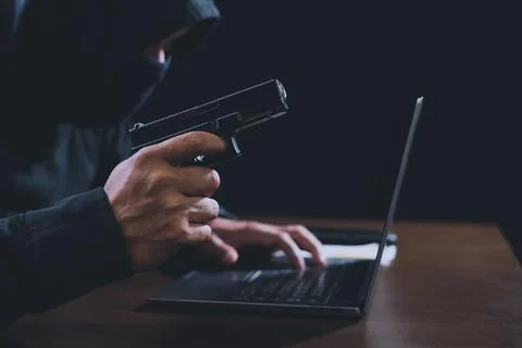 Hacker holding gun and using laptop for hacking passwords of computer system. Foto stock