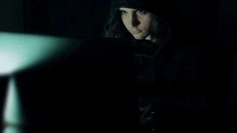 Hacker in hood cracking code using laptop  from his dark hacker room. Stock Footage 73810907
